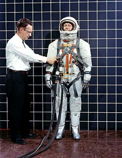 Vemos un hombre con un traje espacial platiado y un hombre al lado en traje corriente le hace una prueba a su traje 